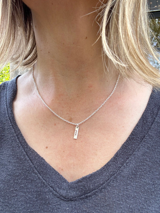 Close up of silver tag style charm with "FUCK" cut into worn on a delicate silver chain.