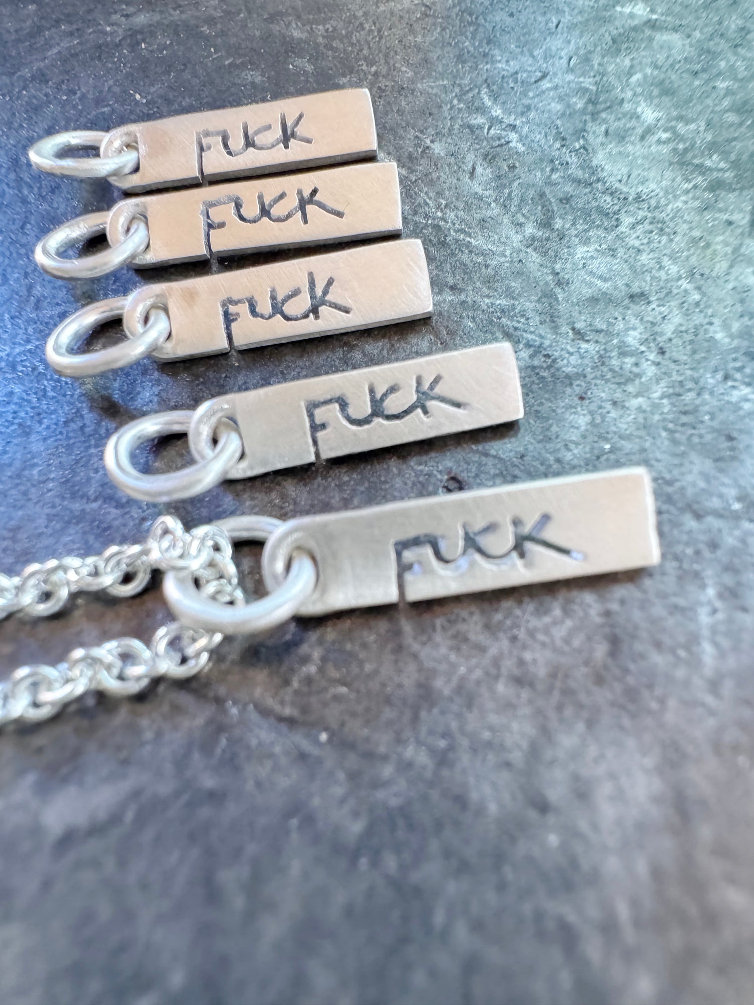 Row of silver tag style charms with "FUCK" cut into them.